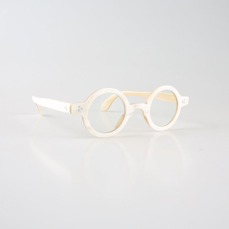 K&ouml;nnte beinhalten: Wei&szlig;e runde Brille mit cremefarbenem Rahmen. Die Brille hat ein schlichtes Design und ist aus leichtem Material gefertigt.