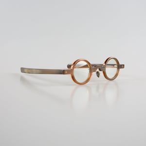 May include: Round, brown tortoiseshell eyeglasses with clear lenses and a grey metal temple.
