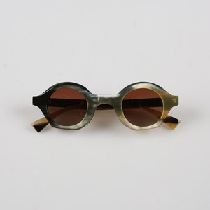 May include: Round tortoiseshell sunglasses with brown lenses. The sunglasses have a black and green pattern on the frames.