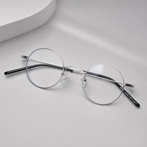 May include: Round spectacles featuring a thin, silver-toned metal frame with clear lenses. The temples are tipped with black plastic ends. Printed on the inner temple is the text SK707 43022-145 CE, indicating the frame specifications.