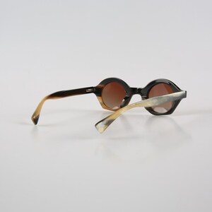 May include: A pair of round, horn-rimmed sunglasses with brown lenses. The frames are a mix of dark brown and light brown.