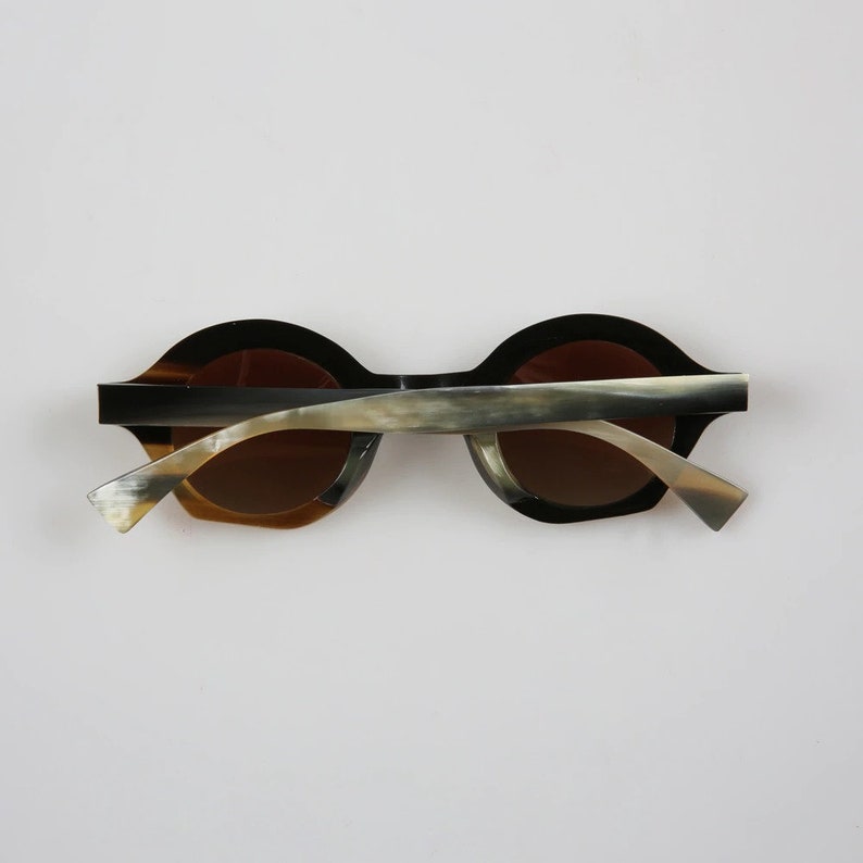 May include: A pair of round horn-rimmed sunglasses with brown lenses. The frames are made of a dark brown and light brown horn material.