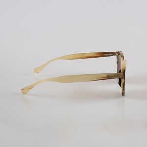 May include: A pair of tortoiseshell sunglasses with a brown frame and brown lenses. The sunglasses are on a white background.