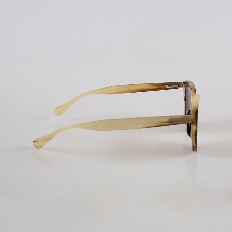 May include: A pair of tortoiseshell sunglasses with a brown frame and brown lenses. The sunglasses are on a white background.