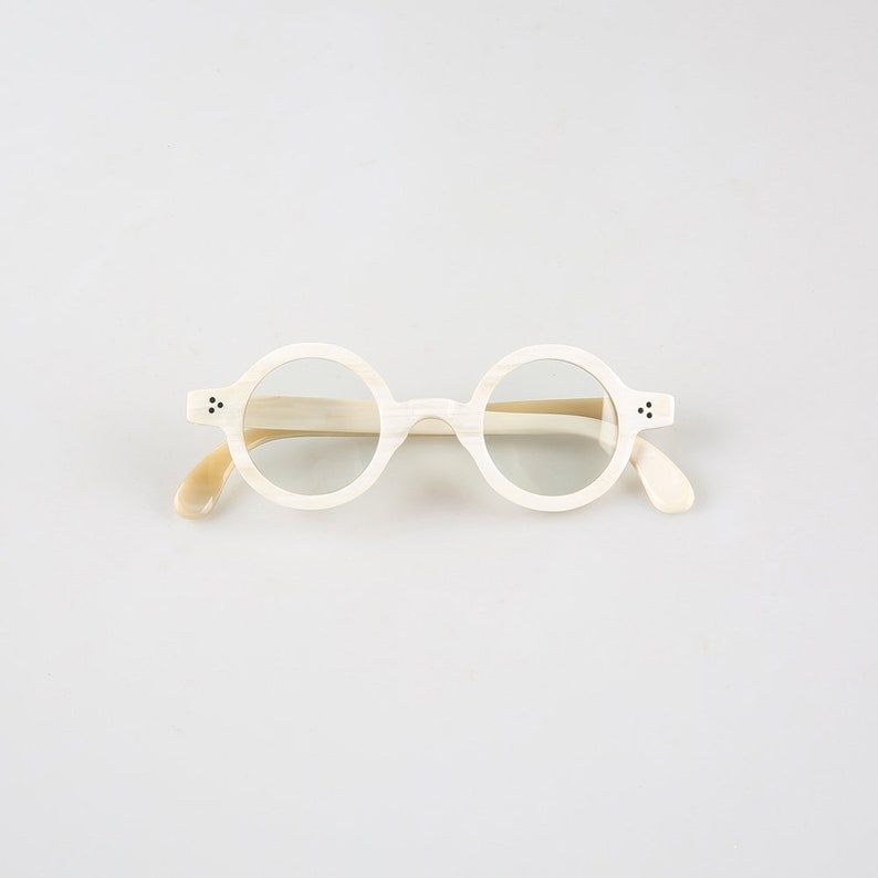 K&ouml;nnte beinhalten: Wei&szlig;e runde Brille mit cremefarbenem Rahmen.