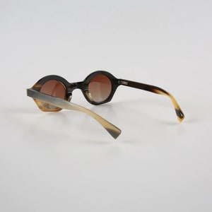 May include: Brown and beige tortoiseshell sunglasses with round lenses. The sunglasses have a unique shape and a modern design.