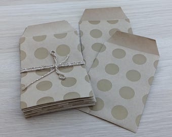 May include: A stack of light brown paper envelopes featuring a repeating pattern of tan polka dots. The stack is secured with a thin, metallic silver string tied in a bow. Two additional matching envelopes are placed beside the stack.