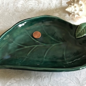 May include: A green ceramic leaf-shaped dish with a raised leaf detail on one side. The dish is glazed and has a glossy finish.