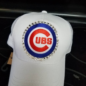 May include: White baseball cap with a blue and red embroidered Chicago Cubs logo surrounded by rhinestones.