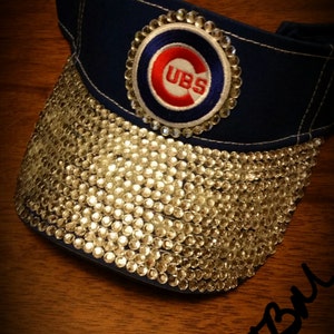 May include: A blue baseball visor with a white and red "CUBS" logo and a bedazzled brim.