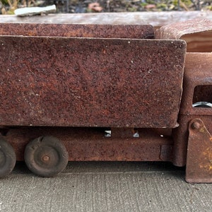 May include: A rusty metal toy dump truck with a yellow scoop. The truck has a bed that lifts up and down. The truck is in good condition, but shows signs of wear and tear.