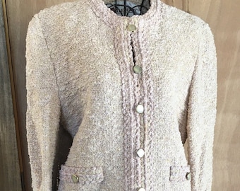 May include: A light pink tweed skirt suit with gold buttons. The jacket has a mandarin collar and long sleeves. The skirt is knee-length.