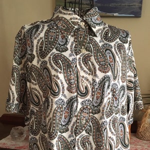 May include: A white short-sleeved button-down shirt with a paisley pattern in shades of brown, green, and blue.
