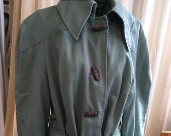 May include: A light blue, belted, long-sleeved jacket with a collar and three wooden toggle closures.