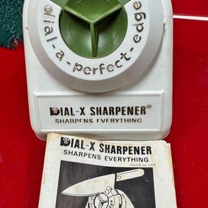 May include: A white and green Dial-X sharpener with the text "Dial-a-perfect-edge" and "Sharpens Everything". Includes a black and white instruction sheet with a knife and scissors graphic.