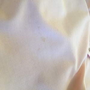 May include: Close-up of a pale yellow fabric with subtle texture and slight discoloration. The fabric appears to be smooth and possibly part of a garment or textile item. The image highlights the material's color and surface details.
