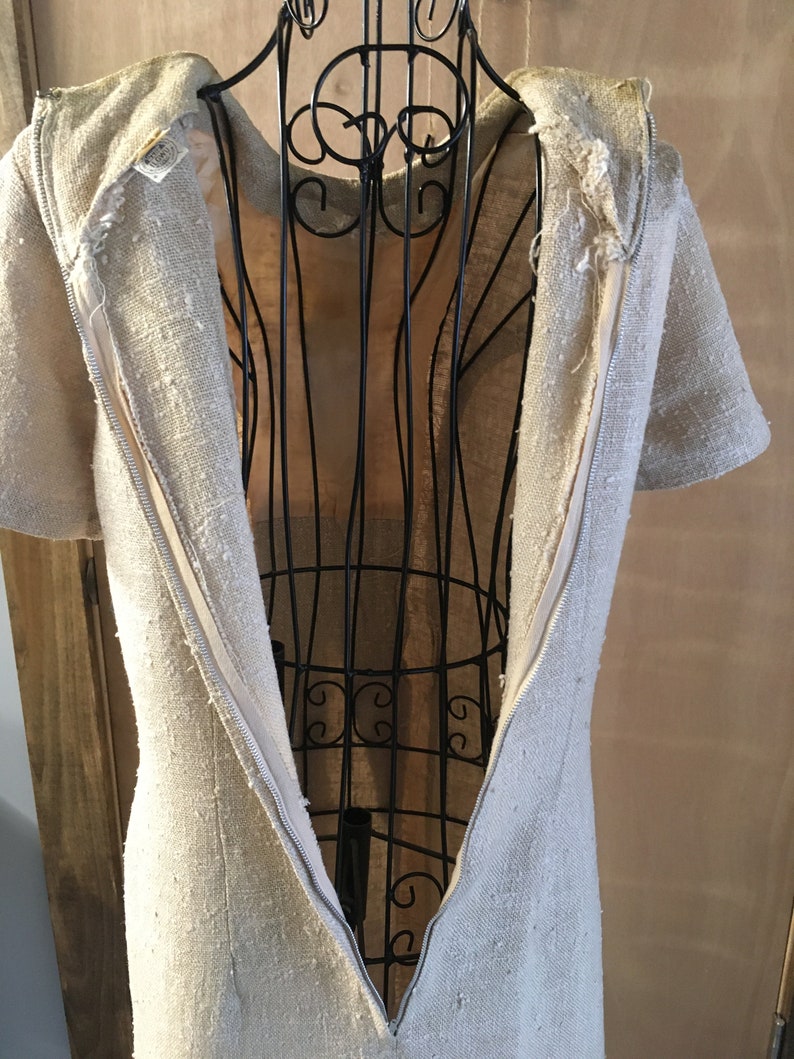 Puede incluir: Un vestido de lino beige con una cremallera en la espalda. El vestido est&aacute; en un maniqu&iacute;.