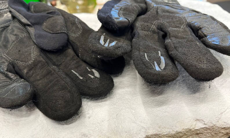以下が含まれることがあります： グレーのアクセントが付いた黒い革の手袋のペア。手袋は質感のある表面を持ち、屋外での活動のために設計されています。