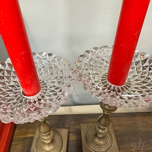 May include: Two vintage candle holders with red candles. The candle holders have a clear, diamond-patterned glass bowl and a brass base. The candles are a bright red color, and the overall aesthetic is classic and elegant.