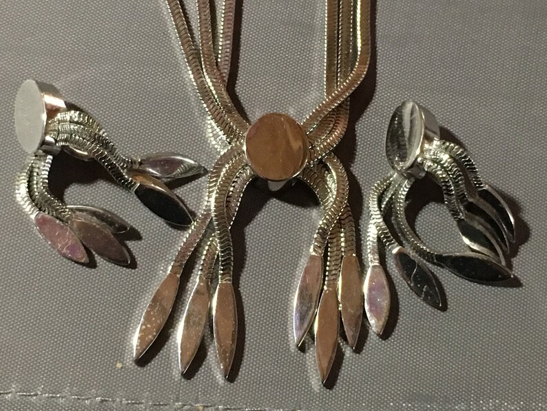 May include: A silver tone necklace and earrings set with a chain link design and dangling leaf-shaped charms.