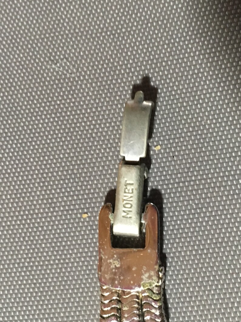 May include: A silver metal watch band with a clasp that says "MONET" on it.