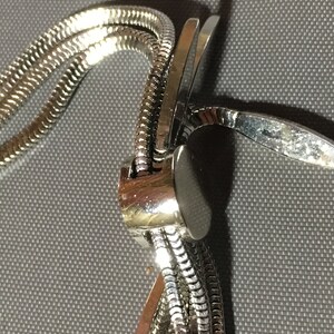 May include: A silver chain necklace with a clasp that is made of multiple interwoven strands.