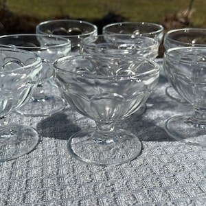 May include: A set of seven clear glass dessert dishes with a fluted design. The dishes have a round bowl and a short stem.