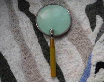 May include: A vintage hand mirror with a round, silver-rimmed magnifying glass and a yellow plastic handle.