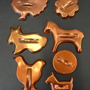 May include: Set of seven copper cookie cutters in various shapes, including a turkey, a horse, a chicken, a rabbit, a dog, a circle, and a flower. The cutters have a copper finish and are designed for baking.