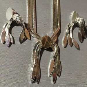 May include: A silver tone necklace and earrings set with a chain link design and leaf-shaped accents.