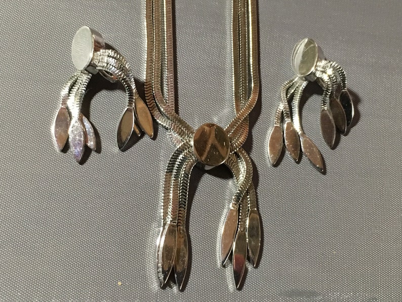 May include: A silver tone necklace and earrings set with a chain link design and leaf-shaped accents.