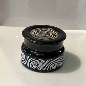 May include: Black ceramic jar with a white and black paisley design. The lid has a gold trim and a black and white paisley design.