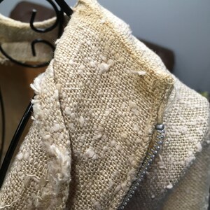 Puede incluir: Primer plano de una chaqueta de lino beige con cremallera. La tela tiene una textura ligeramente peluda.