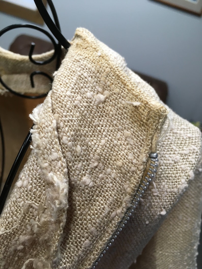 Puede incluir: Primer plano de una chaqueta de lino beige con cremallera. La tela tiene una textura ligeramente peluda.