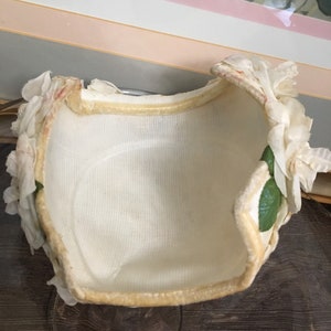 May include: A white fabric hat with a cream colored velvet trim and white fabric flowers with green leaves.
