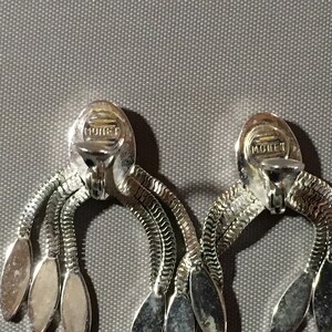 May include: A pair of silver tone clip-on earrings with a chain design and oval shaped accents. The earrings are marked "MONET" on the back.