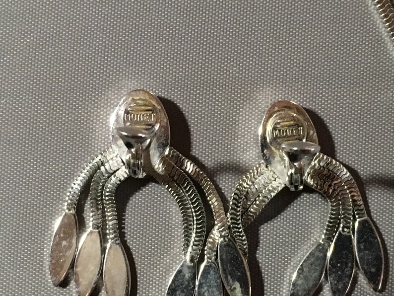 May include: A pair of silver tone clip-on earrings with a chain design and oval shaped accents. The earrings are marked "MONET" on the back.