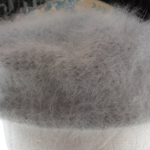 May include: A fluffy gray hat made of soft, fuzzy material. The hat is a light gray color and has a soft, fuzzy texture.