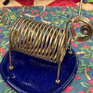 May include: A gold metal wire dog figurine with a coiled spring body and a blue ceramic base.