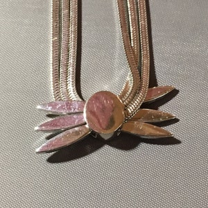 May include: A silver chain necklace with a silver flower pendant. The chain is made of multiple strands of silver.