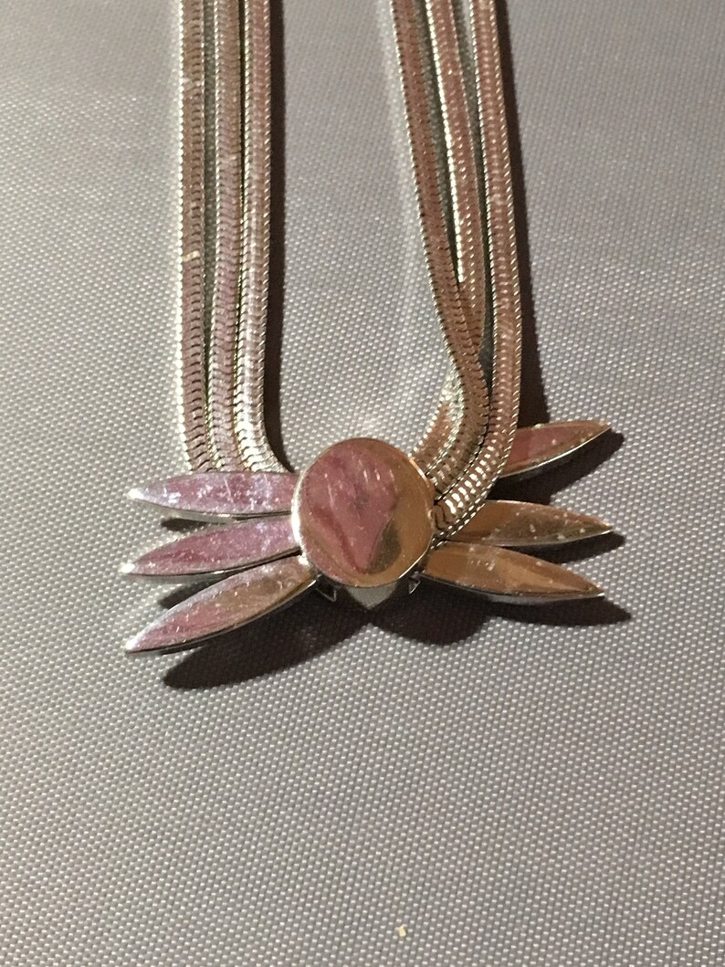 May include: A silver chain necklace with a silver flower pendant. The chain is made of multiple strands of silver.