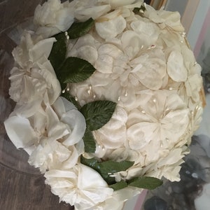 May include: A white fabric hat made of many small flower shapes. The hat is decorated with green leaves and small white beads.