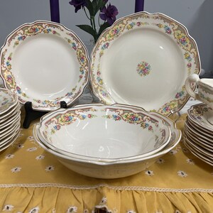 May include: A set of vintage white porcelain dinnerware with floral patterns in shades of pink, yellow, and green. The set includes a large dinner plate, a smaller salad plate, a soup bowl, and a gravy boat.