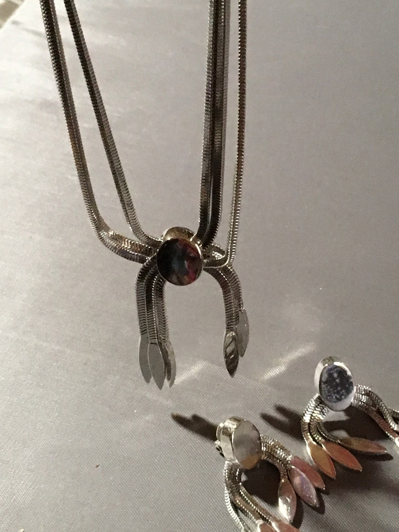May include: A silver necklace and earrings set with a chain link design and a dangling leaf motif.