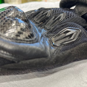 以下が含まれることがあります： カーボンファイバー製のナックルガードとメッシュパネルが付いた、黒い革のオートバイ用グローブです。