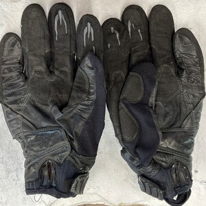 以下が含まれることがあります： 指先に補強と手のひらにパッドが付いた、黒色の革製のオートバイ用グローブのペアです。