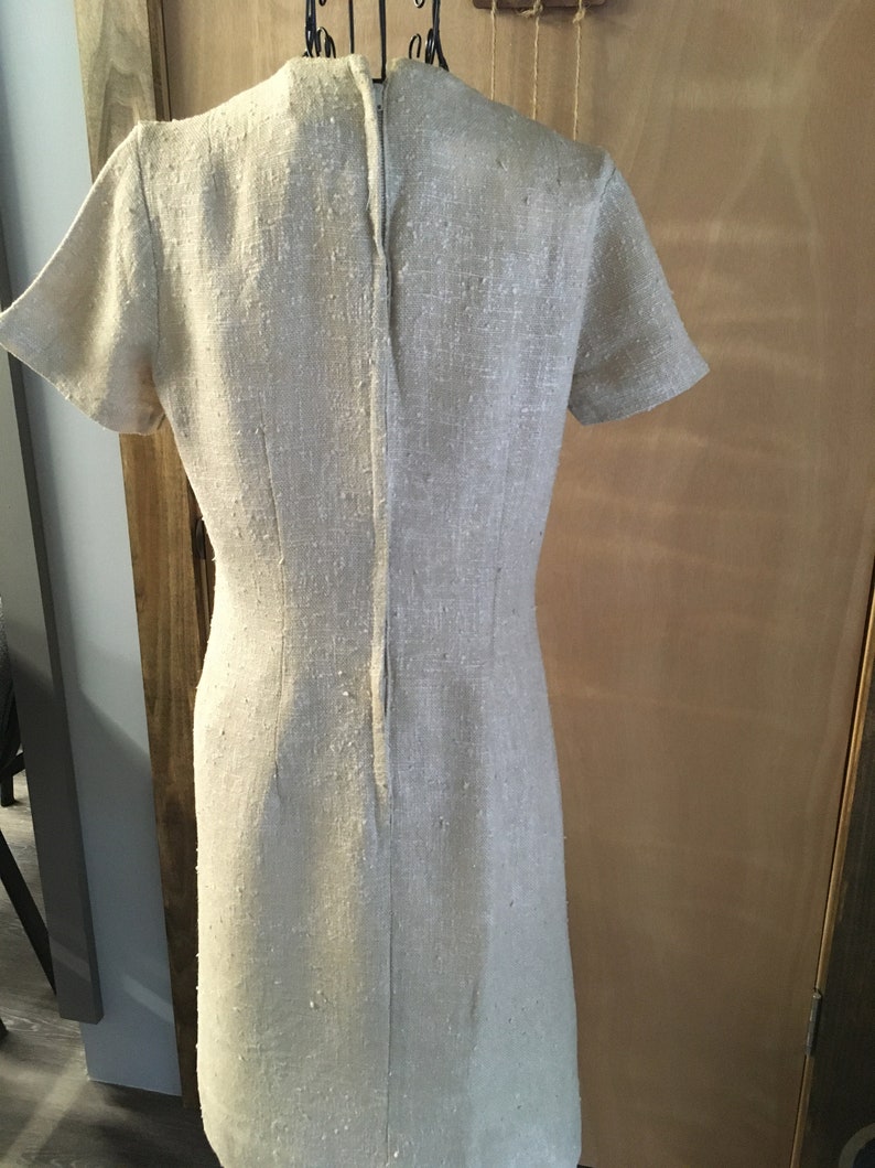 Puede incluir: Un vestido de lino beige con mangas cortas y una cremallera en la espalda.