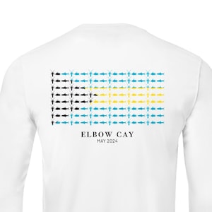May include: White long-sleeve shirt with a graphic of a row of fish in blue, yellow, and black colors. The text "ELBOW CAY MAY 2024" is printed below the graphic.
