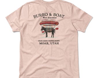 May include: Light pink t-shirt with a graphic of a donkey carrying a boat and paddles. The text "BURRO & BOAT River Expeditions" is above the graphic. Below the graphic is the text "PACK LIGHT. PADDLE HARD. MOAB, UTAH."
