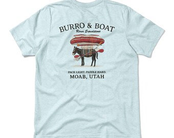 May include: Light blue t-shirt with a graphic featuring a mule carrying a boat and paddles. The text "BURRO & BOAT River Expeditions" is above the illustration. Below the illustration, the text reads "PACK LIGHT. PADDLE HARD. MOAB, UTAH."